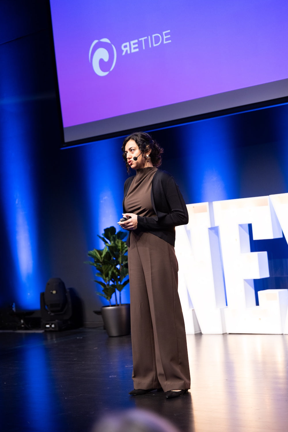 Parisa giving a presentation on a stage with 'Retide' branding in the background
